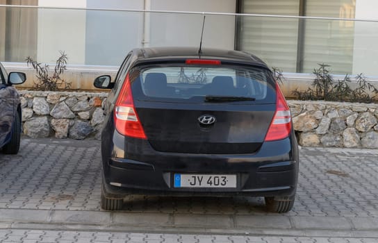 Gaziveren Cyprus -30.01.2025 A black hatchback rests against a stone wall, basking in the warm midday sun, creating a serene atmosphere.