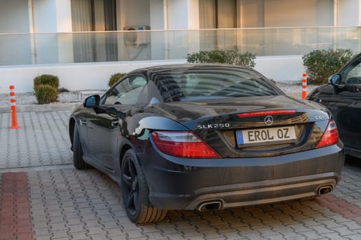 Gaziveren Cyprus -30.01.2025 A luxurious black convertible is parked in a charming courtyard as the sun sets, casting a warm glow.