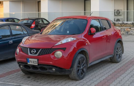 Gaziveren Cyprus -30.01.2025 A vibrant red compact vehicle stands still on cobblestones, showcasing slightly dusty surfaces in early evening light.