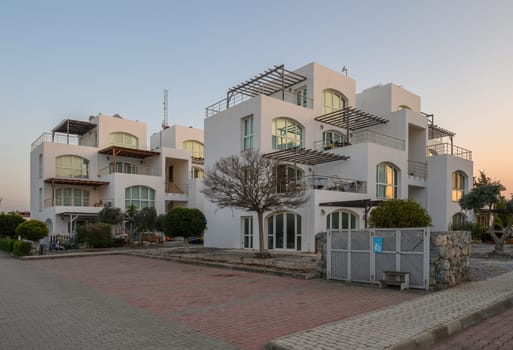 Charming white buildings adorned with balconies emerge amid lush greenery as twilight casts a warm glow.
