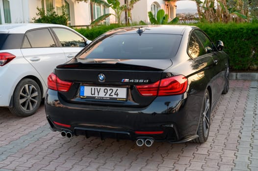 Gaziveren Cyprus -30.01.2025 A sleek black sports car rests elegantly in a vibrant parking area, surrounded by lush plants and warm light.