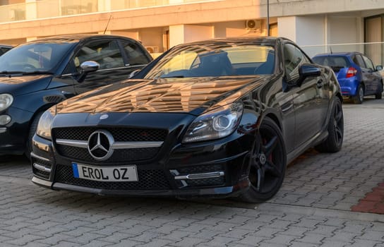 Gaziveren Cyprus -30.01.2025 A stylish black sports car stands proudly in a parking space, reflecting warm colors from the setting sun.