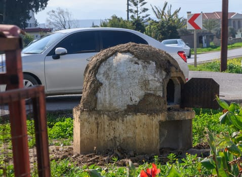 A charming rustic oven made of natural materials sits by the roadside, surrounded by lush greenery and vibrant flowers.