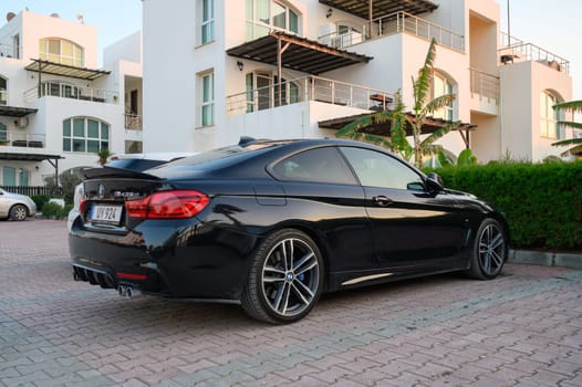 Gaziveren Cyprus -30.01.2025 A stylish black coupe rests quietly in front of a contemporary building, bathed in warm evening sunlight.