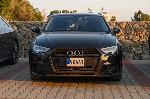 Gaziveren Cyprus -30.01.2025 A sleek black luxury sedan stands parked beside a rugged stone wall under the warm glow of the setting sun.