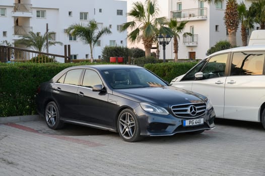 Gaziveren Cyprus -30.01.2025 A sleek luxury sedan rests in a modern lot, surrounded by lush palm trees and stylish buildings as the sun sets.