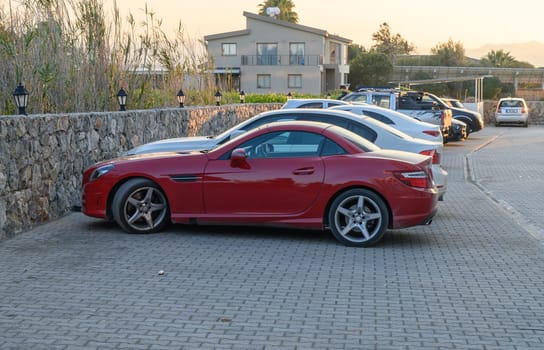 Gaziveren Cyprus -30.01.2025 A stunning red sports car parked beside sleek vehicles in a tranquil setting at sunset, surrounded by greenery.