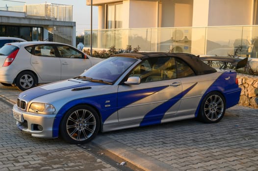 Gaziveren Cyprus -30.01.2025 A vibrant convertible in a coastal lot basks in the sunset, highlighting its custom paint.