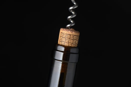 A close-up view shows a corkscrew pulling a cork from a wine bottle, highlighting rich textures and tones.