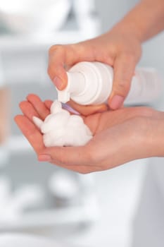 Crop cosmetologist hand carefully removing foam cream from bottle into their hand at clinic, showcasing professional and gentle skincare treatment in progress