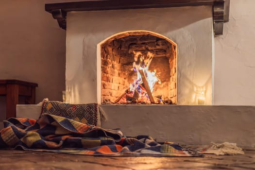 A warm and inviting scene featuring a lit fireplace with glowing firewood and candles. A colorful traditional rug and pillow lie on the floor, creating a cozy atmosphere. Home, relaxation, and rustic comfort concept.