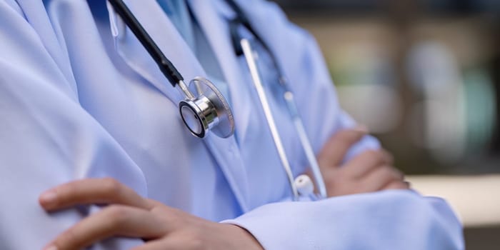Close up of a doctor arms crossed, wearing a white coat and stethoscope, representing professionalism and commitment in the medical field.