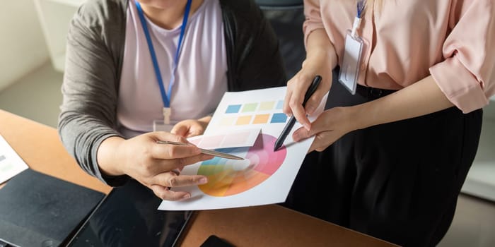 Close-up of two graphic designers examining color swatches and palettes, emphasizing teamwork and creativity in their design process within a vibrant workspace.