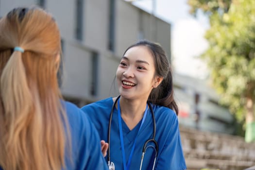 Two doctors in blue scrubs share a cheerful conversation during their break, one with a stethoscope around her neck, highlighting the joy and camaraderie in the healthcare profession.