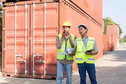 Two engineers in safety gear are coordinating logistics and discussing project plans while standing in front of shipping containers, emphasizing teamwork and effective communication.