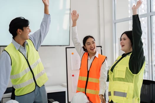 A vibrant construction team of an architect, engineer, and designer raises their hands in joy, celebrating their project's success in a contemporary office space.
