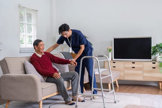 A nurse assists an elderly man in transitioning from his walker to a cozy couch in a sunlit living room, enhancing his comfort and recovery.