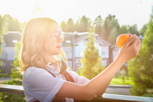 A girl examines a bright orange, basking in sunlight, surrounded by trees and homes during a serene afternoon.