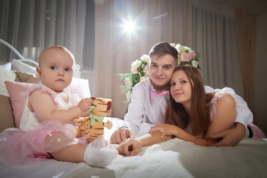 A couple enjoys a tender moment while their baby girl plays with a toy in a warm, inviting space filled with soft lighting on bed in beautiful room