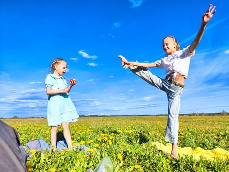 Two girls are playing in a bright field, surrounded by blooming flowers, with one striking a joyful dance pose next to the other.