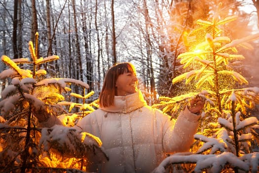 A middle-aged woman walks joyfully through a snowy forest, surrounded by trees blanketed in snow, celebrating the winter season.