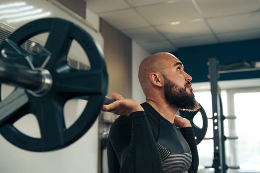 A man is performing a weightlifting exercise in a gym, focusing intently as he lifts a barbell. The environment is bright and equipped with fitness gear.