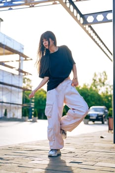 A young woman showcases her dance moves in an urban area, surrounded by construction and greenery, as the warm glow of golden hour enhances the atmosphere.