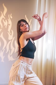 A dancer performs gracefully in a well-lit indoor area, highlighting her fluid movements against an interesting background of abstract shadows and soft curtains.