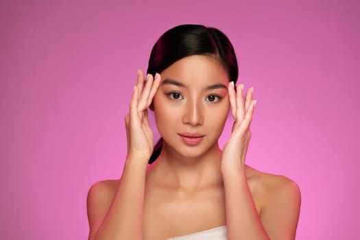 A model demonstrates poise and confidence while positioning her hands delicately near her face. The vibrant pink background enhances her beauty, creating a striking visual contrast.