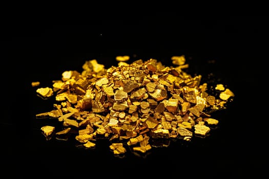 Pile of shiny raw gold nuggets on black background.