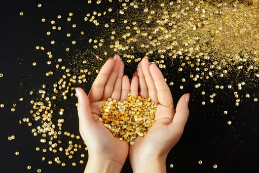 Close-up of hands holding shimmering gold glitter against black background.