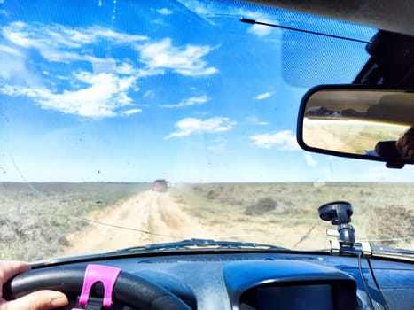 A driver navigates an open road with a cracked windshield while surrounded by green fields and a bright blue sky filled with clouds.