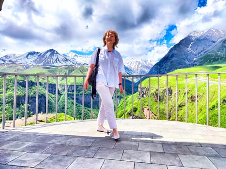 A woman is gracefully standing on a beautiful balcony that overlooks a stunning mountain range, enjoying the breathtaking view ahead