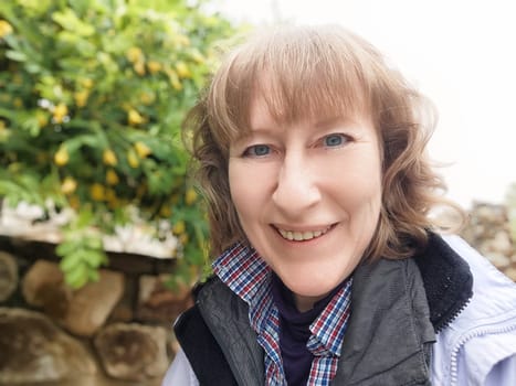 Middle-aged woman enjoys taking selfies in a park, embracing nature during her exciting travel journey.