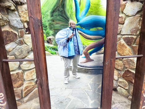 A modern woman captures a humorous selfie in a warped mirror while exploring a scenic park on her journey.