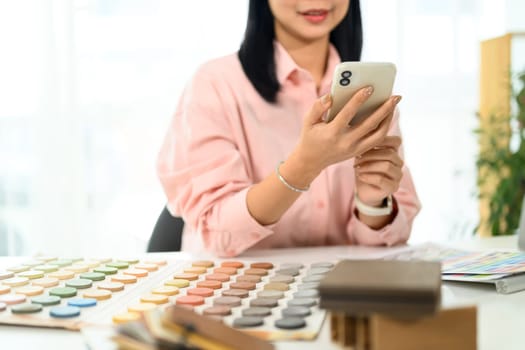 Smiling creative woman reviewing design inspirations on her smartphone at office desk.