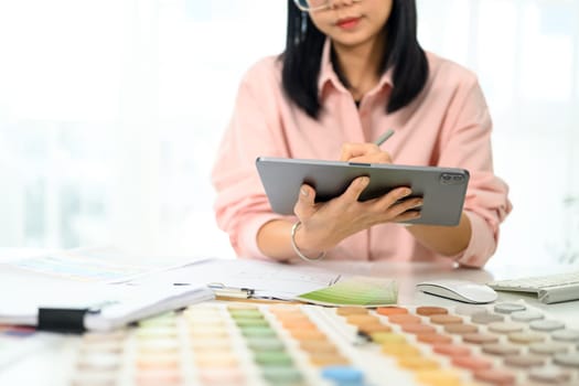 Young female designer working on a digital tablet analyzing color samples and design plans.