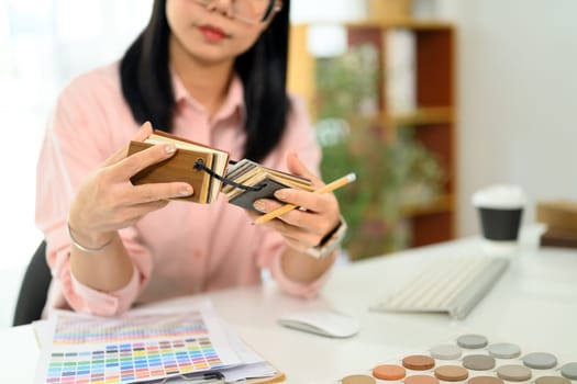 Cropped shot decorator choosing laminate floor samples at desk. Home design and renovation.