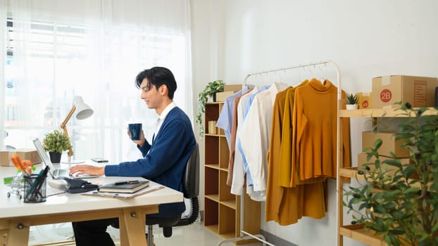 Freelancer working on his laptop, surrounded by clothing samples and neatly stacked packages.