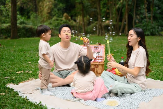 Happy family enjoys a relaxing picnic in a lush green park and blowing bubbles together.