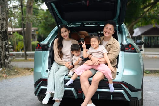 Cheerful family sitting in the open trunk of their car, enjoying a break during their road trip.