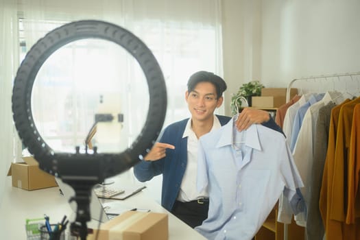 Confident online retailer presenting shirts in front of smartphone camera.