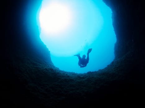 silhouette of unrecognizable scuba diver diving in the hole of a dark cave undersea in deep clear water, concept of active lifestyle at nature and underwater adventure, copyspace for text