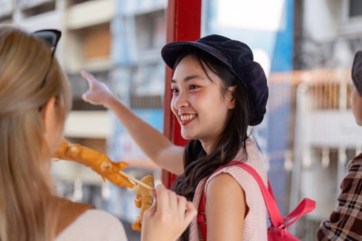 A young Asian woman excitedly pointing while enjoying street food with friends in a vibrant market, showcasing the joy of travel and shared experiences.