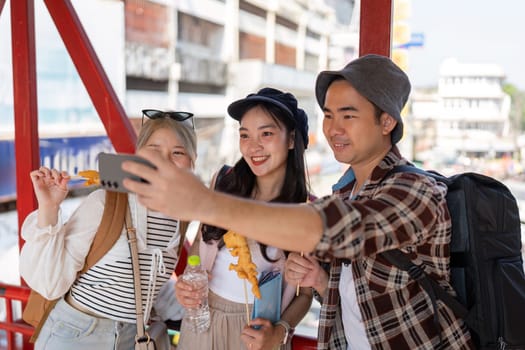 A group of young Asian friends happily taking a selfie with street food in hand, capturing joyful moments in a lively market atmosphere.