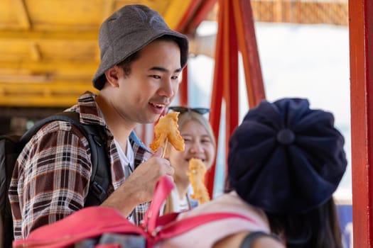A young Asian man animatedly talking with friends while savoring street food in a bustling market, celebrating the joy of travel and connection.