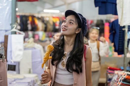 A young Asian woman savoring street food at a lively market, embodying the joy of travel and friendship in a bustling environment.