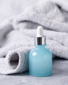 Light blue dropper bottle with pipette near light gray bath towel closeup, brand packaging mockup, copy space. Natural cosmetic product for facecare and spa procedures - serum or essence
