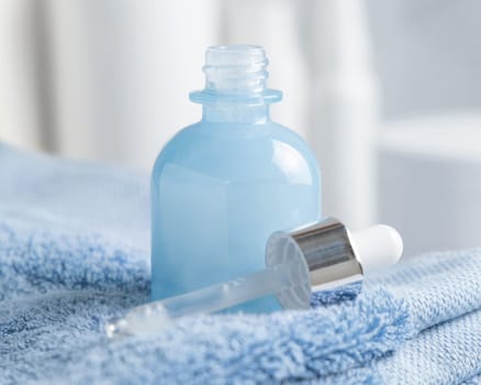 Pipette near a light blue glass dropper bottle close up. Blue folded towel and cosmetics in bathroom, mockup. Natural serum or essence
