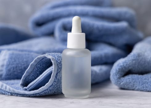 Clear glass dropper bottle with pipette near blue towel closeup, brand packaging mockup, copy space. Natural handmade cosmetic product for facecare and spa procedures - serum or essence